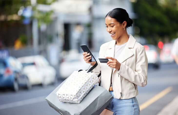 A woman out shopping with bags, her phone, and a credit card in hand.