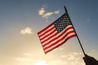 Image of hand holding an American flag with the sky as the background