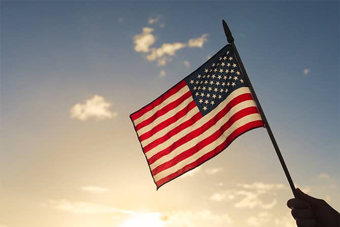 Image of hand holding an American flag with the sky as the background