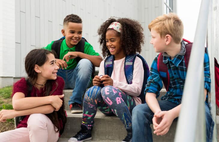 Group of kids sitting and talking on steps outside.