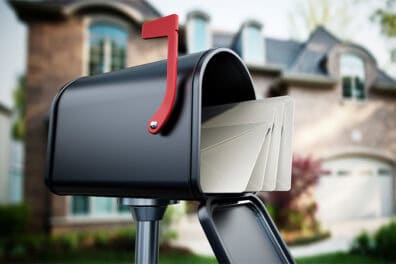 Photo of an open mailbox with mail inside and the flag up. House is blurred in the background.